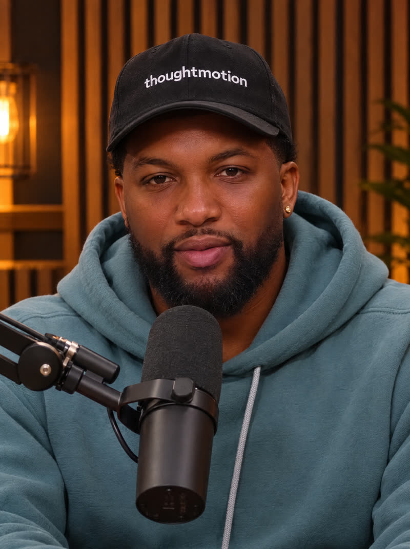 Josh at a podcast microphone in a thoughtmotion cap, looking into the lens, generated from one reference photo